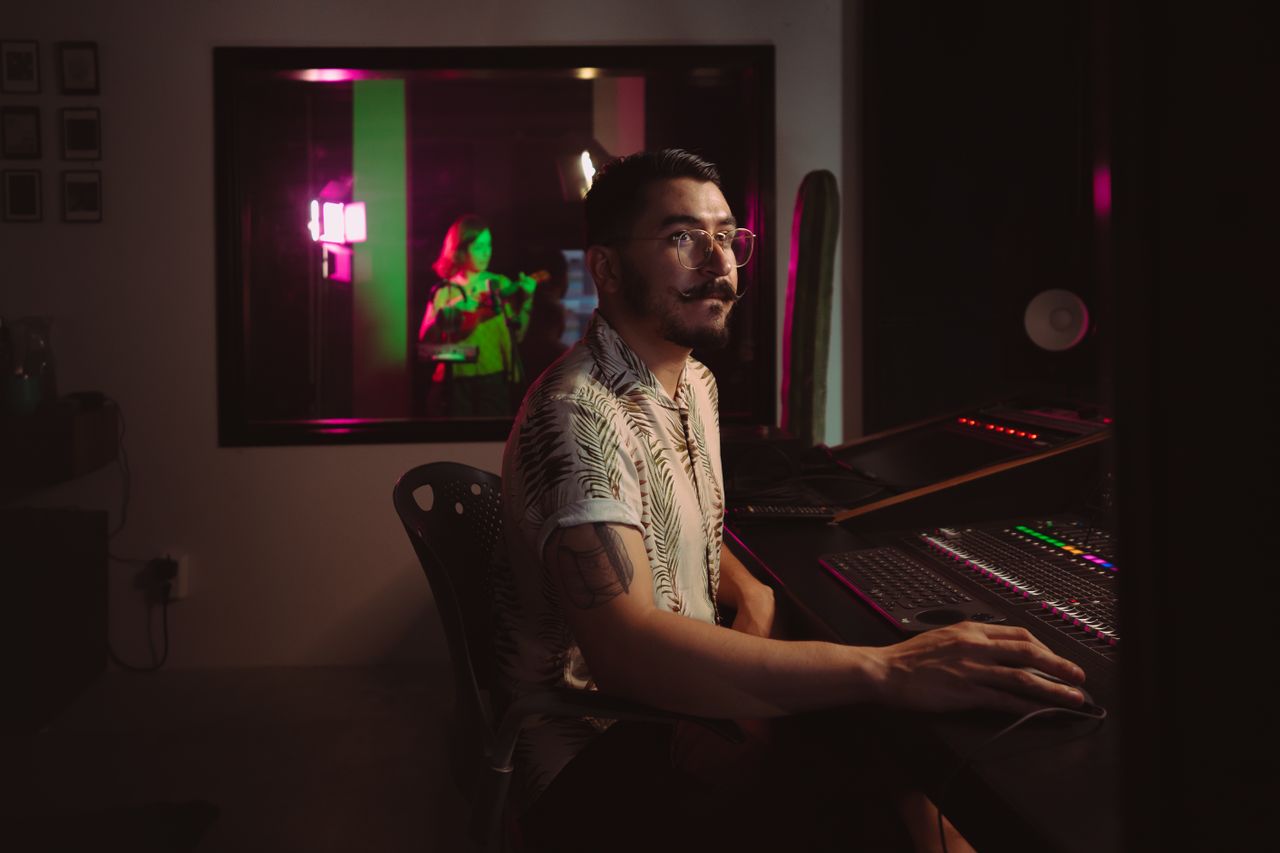 Crafting Captivating Headlines: Your awesome post title goes here Man working at a mixing console in a recording studio with vibrant lighting and tattooed arm.